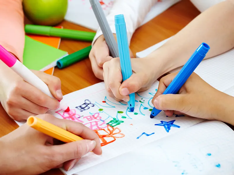 Des mains d'enfants dessinent avec des feutres